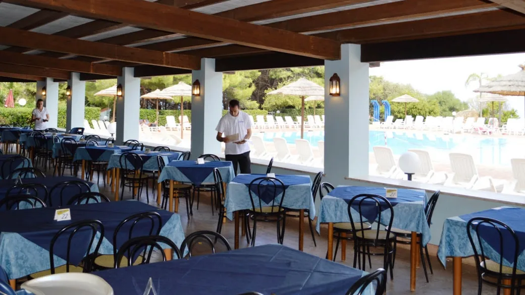 Terrazza ristorante con tavoli dalle tovaglie blu affacciata sulla piscina del resort