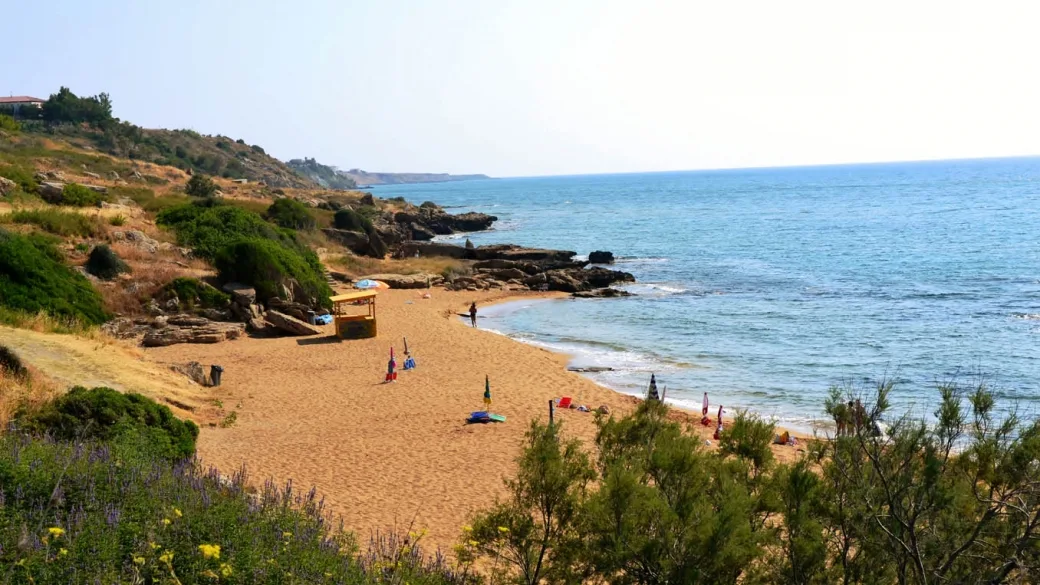 Cala naturale con spiaggia sabbiosa incorniciata da scogli e vegetazione mediterranea