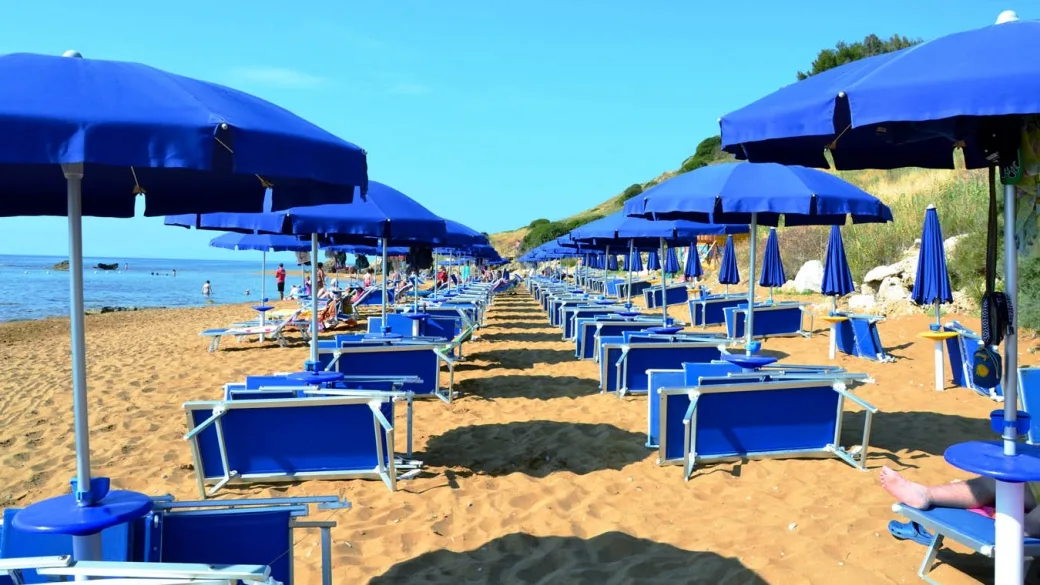 Vista tra le file di ombrelloni blu e lettini sulla spiaggia sabbiosa verso il mare