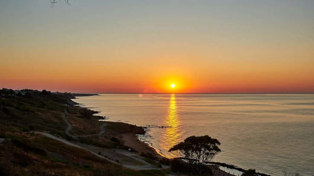 Tramonto suggestivo sul mare con riflesso dorato del sole sull'acqua e costa in ombra