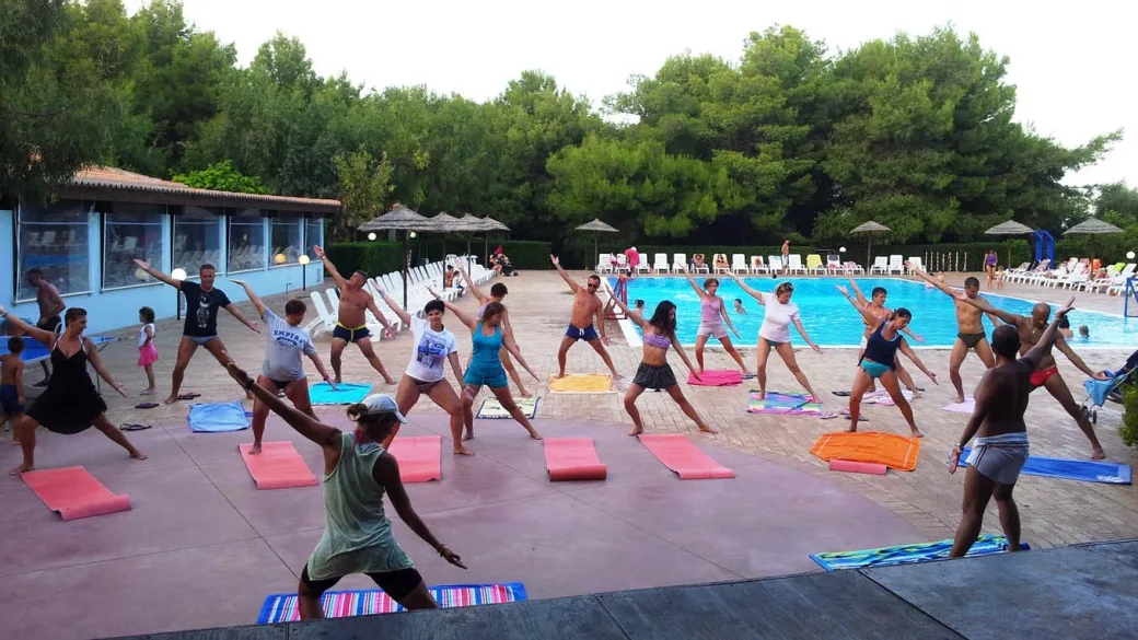 Lezione di ginnastica a bordo piscina con partecipanti su tappetini colorati
