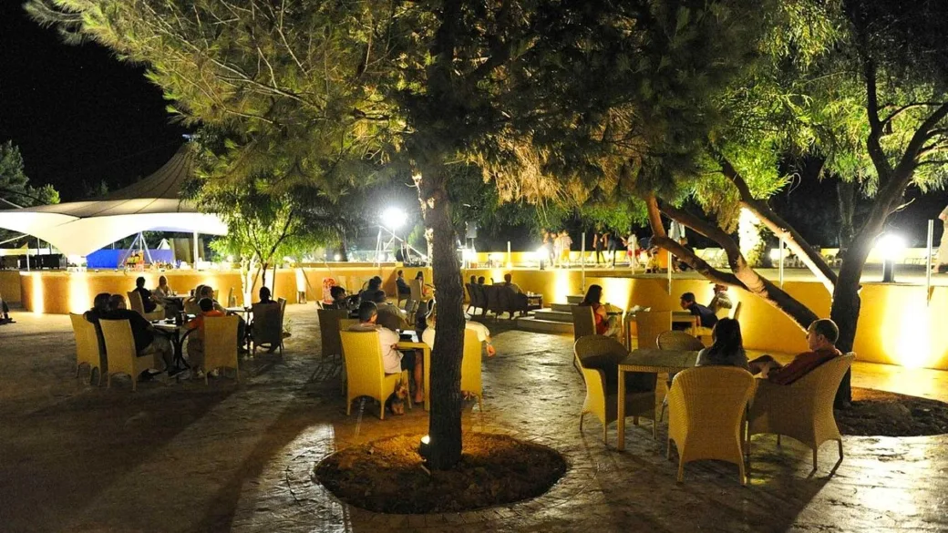 Area ristorante all'aperto illuminata di sera con tavoli e alberi