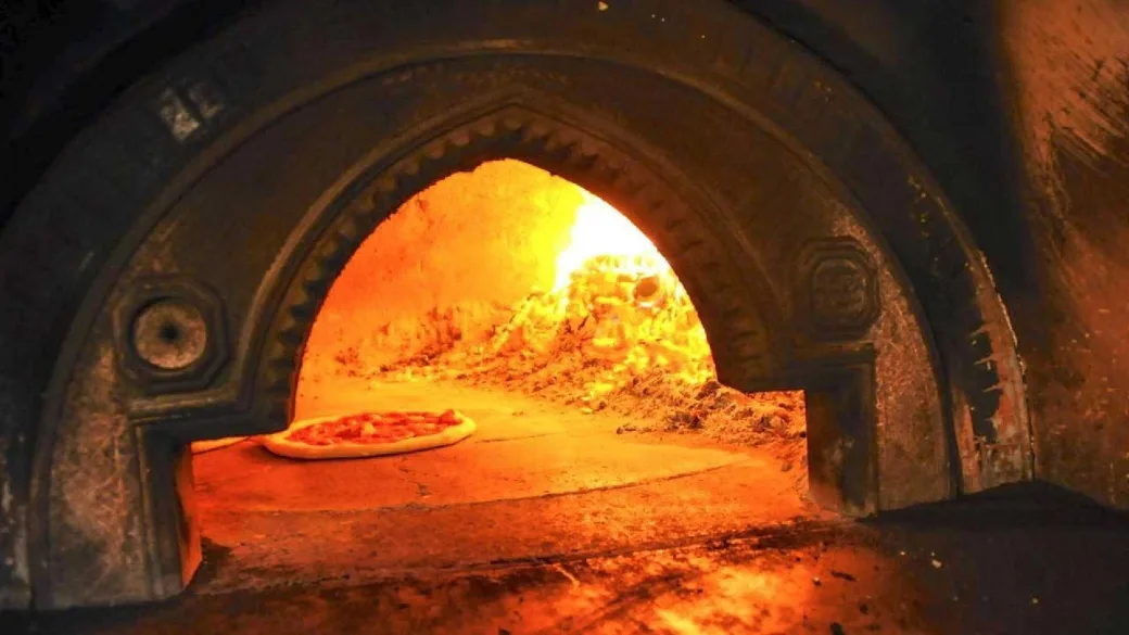Pizza in cottura in forno a legna con fiamme accese
