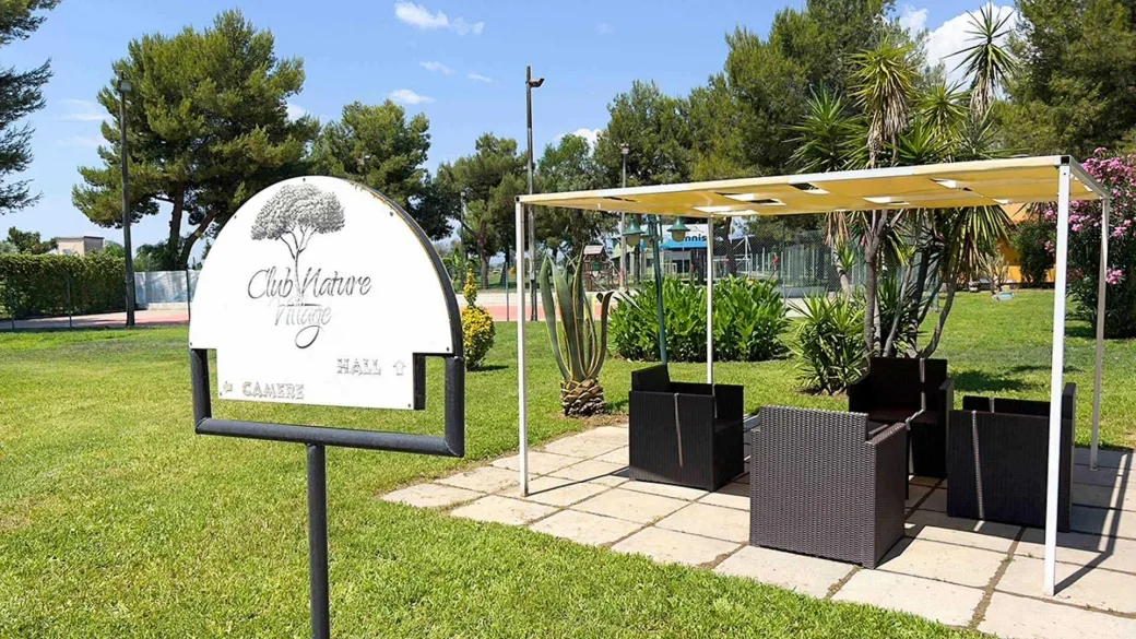 Insegna del Club Nature Village con gazebo e area verde con piante