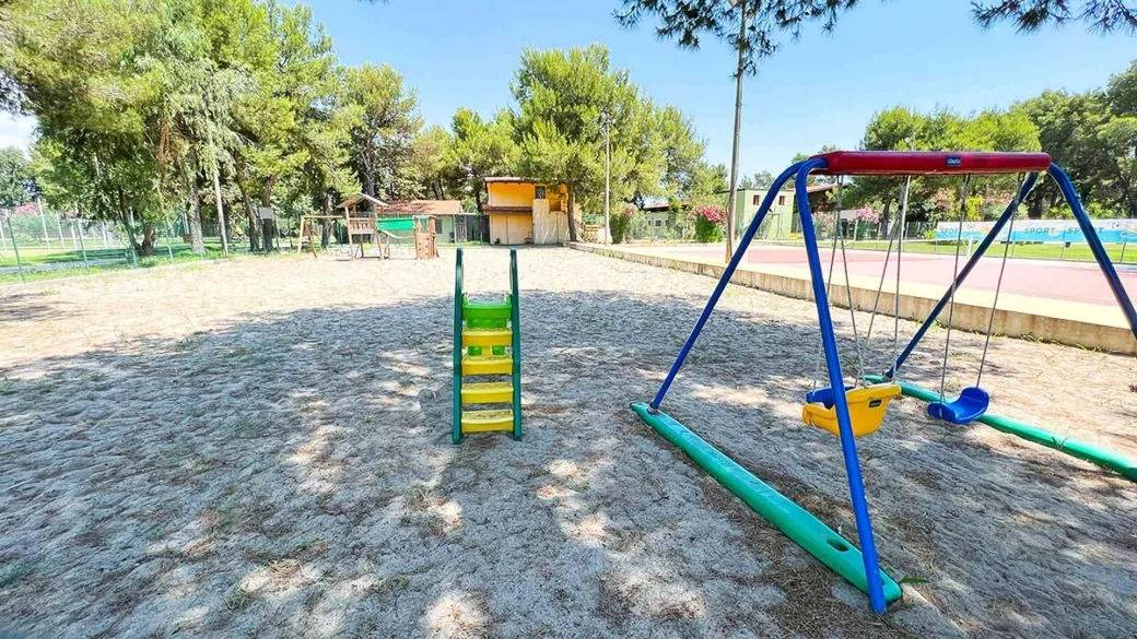 Area giochi per bambini con altalena e scivolo circondata da alberi