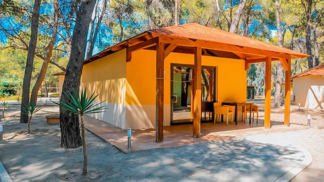 Bungalow giallo con veranda in legno immerso nella pineta