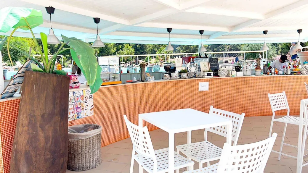 Bar con bancone in mosaico arancione e tavoli bianchi sotto pergola