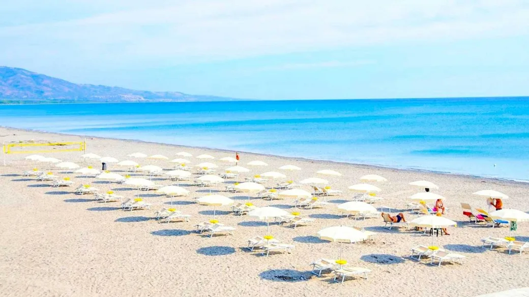Ampia spiaggia sabbiosa con file di ombrelloni e mare azzurro all'orizzonte