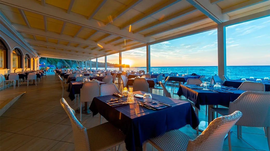 Ristorante sul mare al tramonto con tavoli blu e vista sull'orizzonte