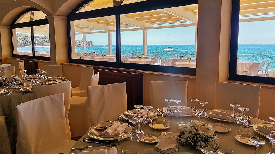 Sala ristorante elegante con tavoli apparecchiati e ampie vetrate sul mare