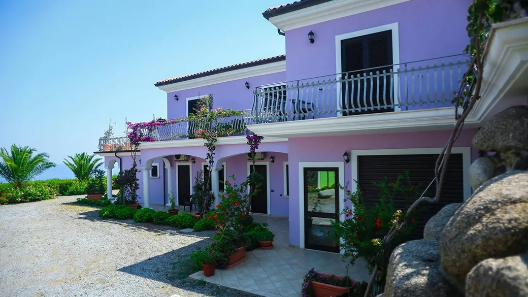 Villa color lilla con archi, balconi e giardino fiorito vista mare