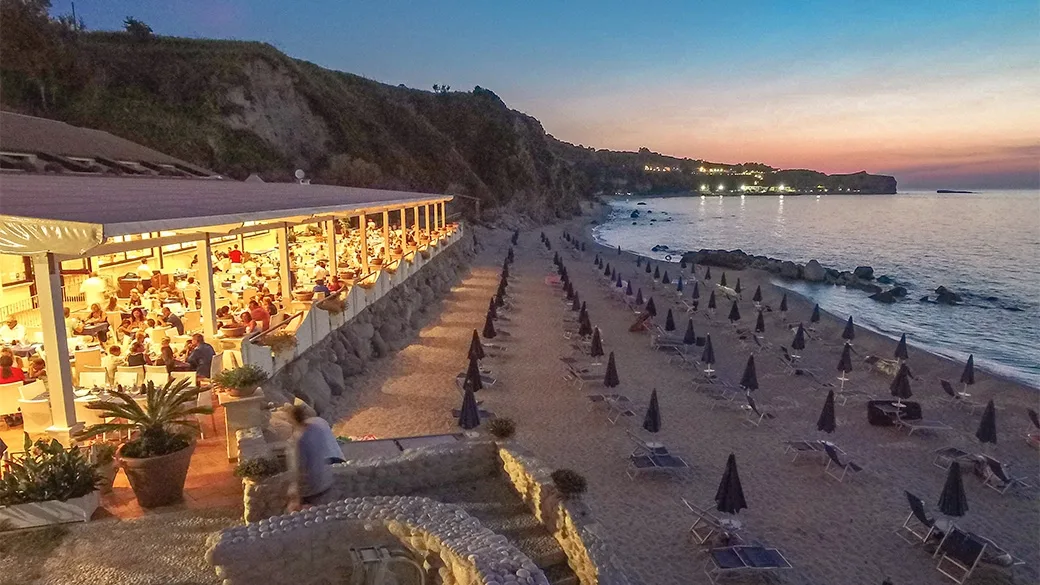 Ristorante affollato sulla spiaggia al tramonto con ombrelloni chiusi