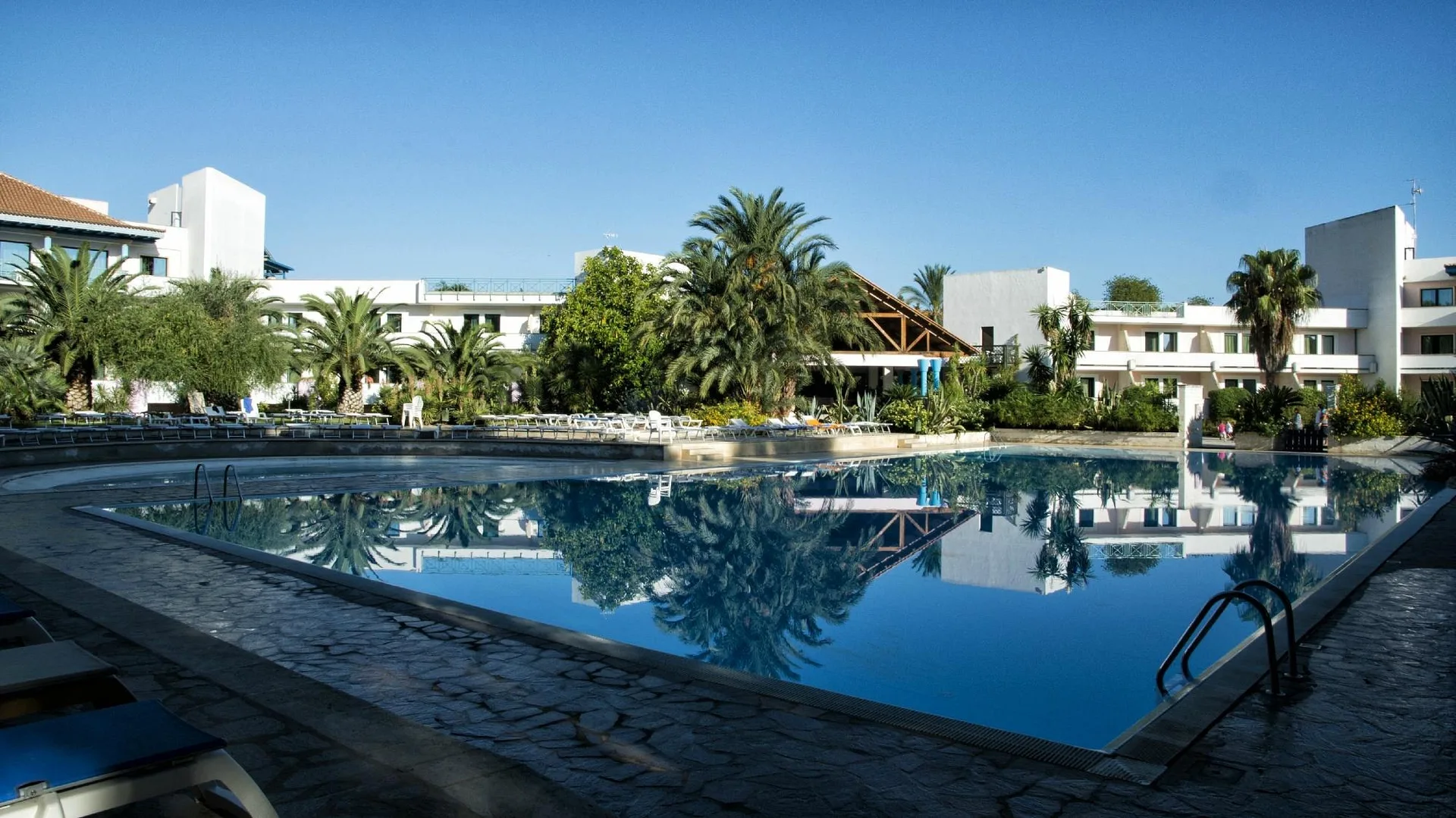 Grande piscina che riflette le palme circondata dagli edifici bianchi dell'hotel