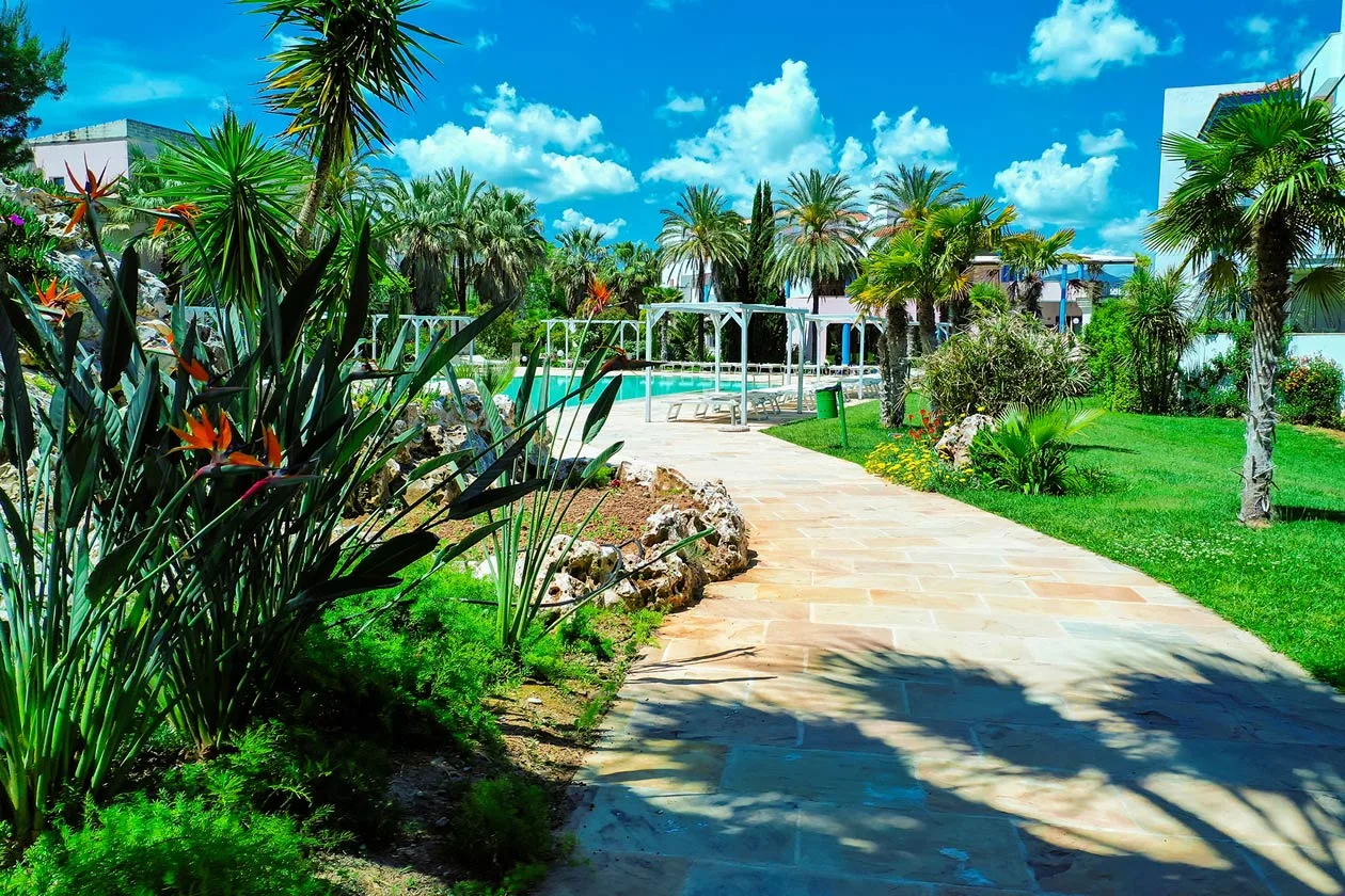 Vialetto in pietra tra giardino tropicale con palme e fiori verso la piscina
