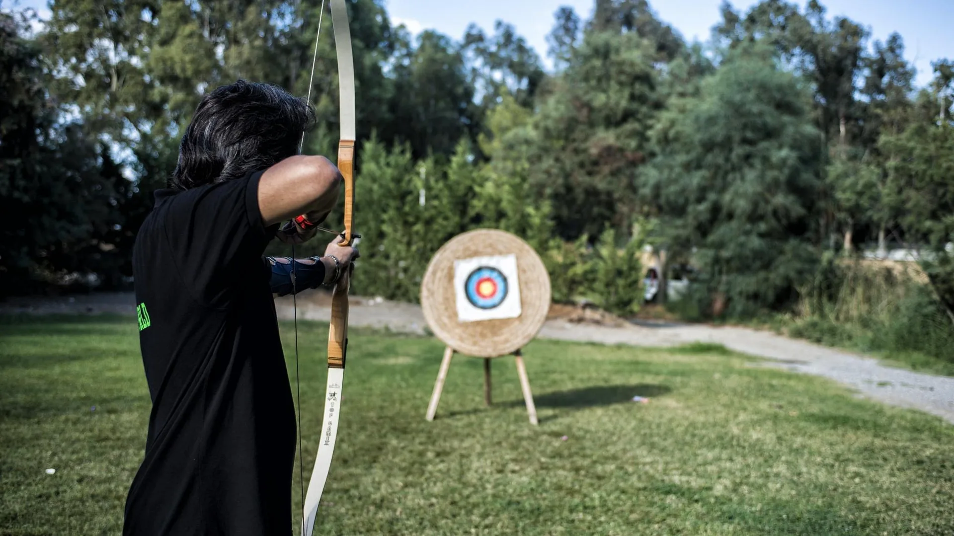 Persona che pratica tiro con l'arco verso un bersaglio in giardino
