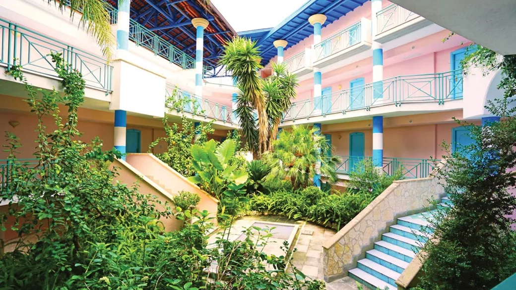 Cortile interno con vegetazione lussureggiante, colonne bianche e azzurre e scale
