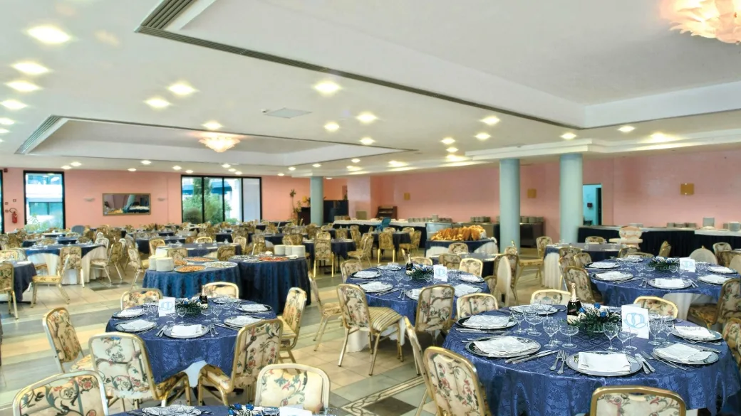 Sala ristorante con tavoli rotondi apparecchiati con tovaglie blu e sedie eleganti