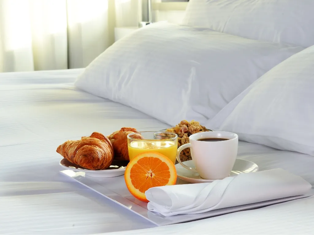 Colazione a letto con croissant, caffè, spremuta d'arancia e cereali su vassoio