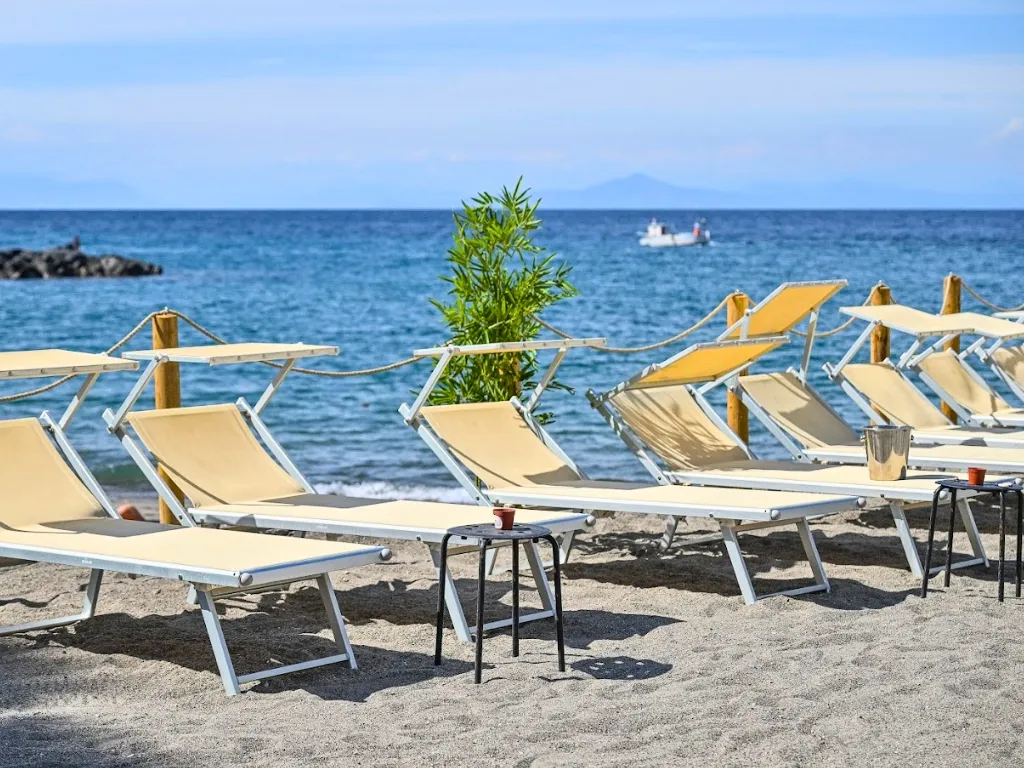 Lettini da spiaggia beige sulla sabbia con vista sul mare e barca all'orizzonte