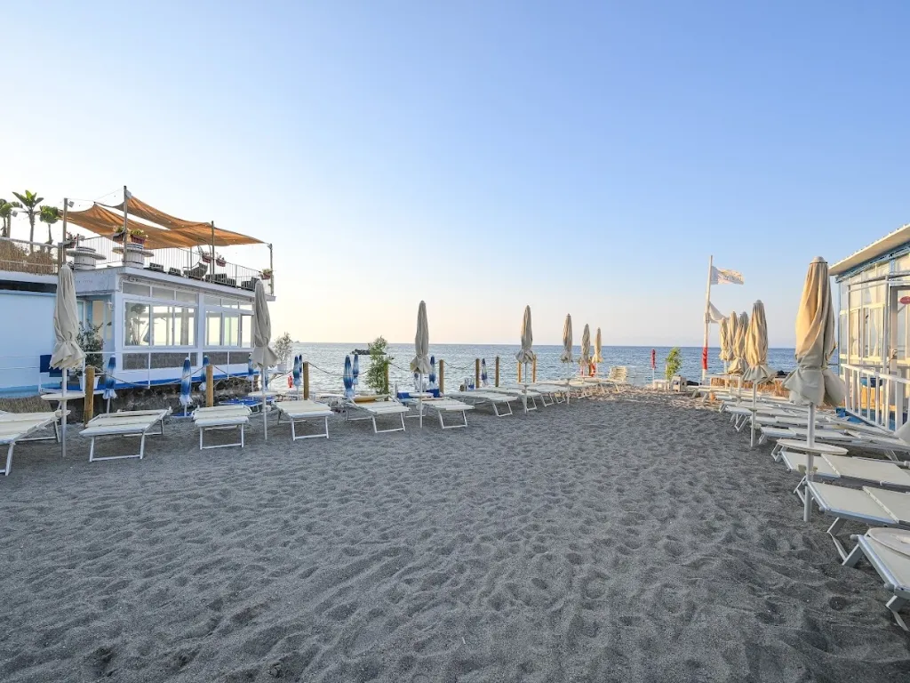 Spiaggia di sabbia con lettini, ombrelloni chiusi e stabilimento balneare sul mare