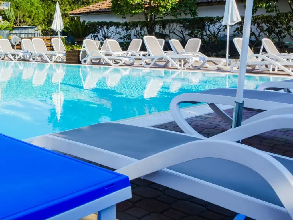 Piscina esterna con lettini bianchi e blu circondata da vegetazione