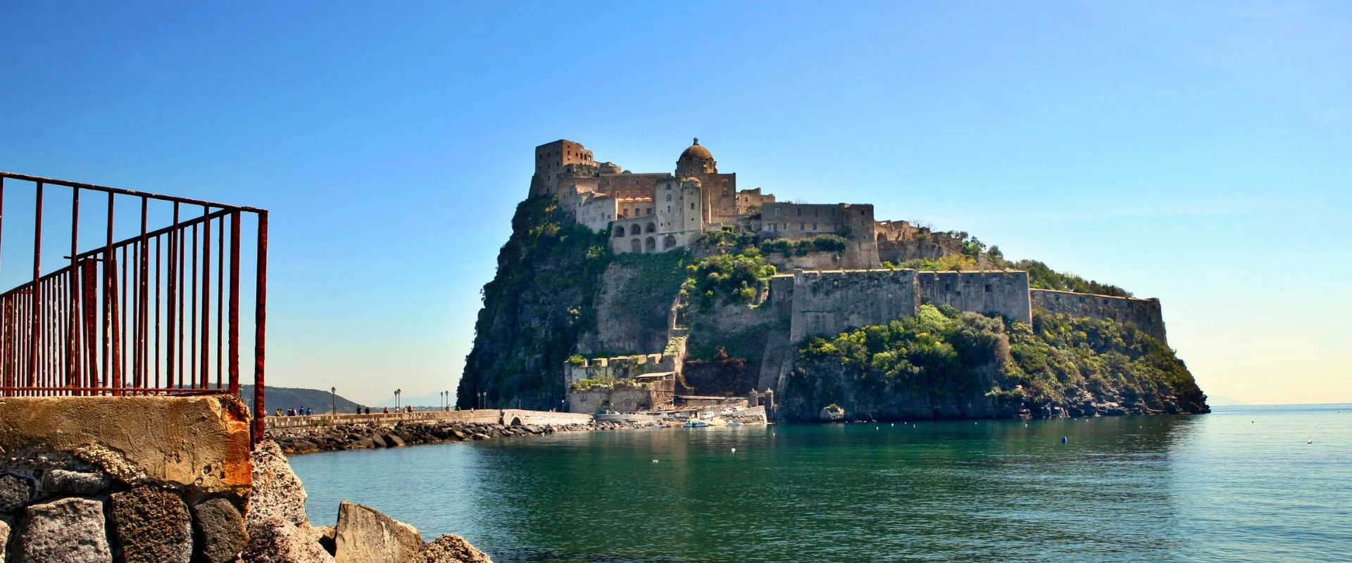 Il Castello Aragonese di Ischia visto dal molo con mare calmo e cielo sereno