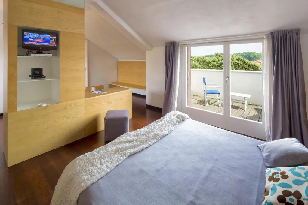 Camera moderna con arredi in legno chiaro, TV, pavimento in parquet e terrazza vista campagna