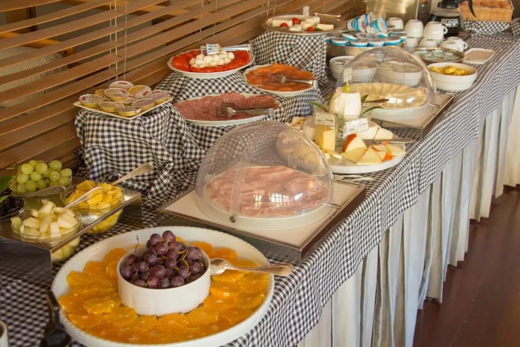 Buffet della colazione con affettati, formaggi, frutta fresca e marmellate su tavolo con tovaglia a quadri