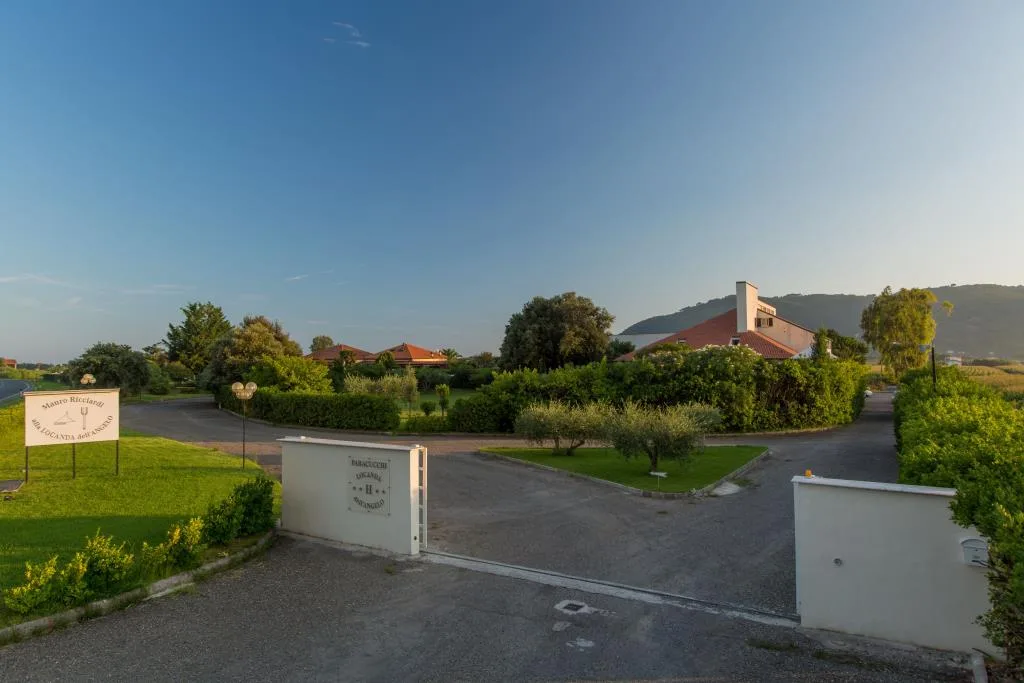 Ingresso della struttura con cancello, giardino curato e collina verde sullo sfondo al tramonto