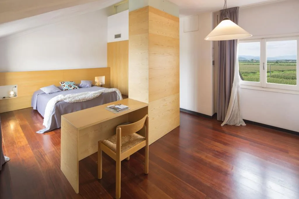 Camera spaziosa con letto matrimoniale, scrivania in legno, pavimento in parquet e vista sulla campagna