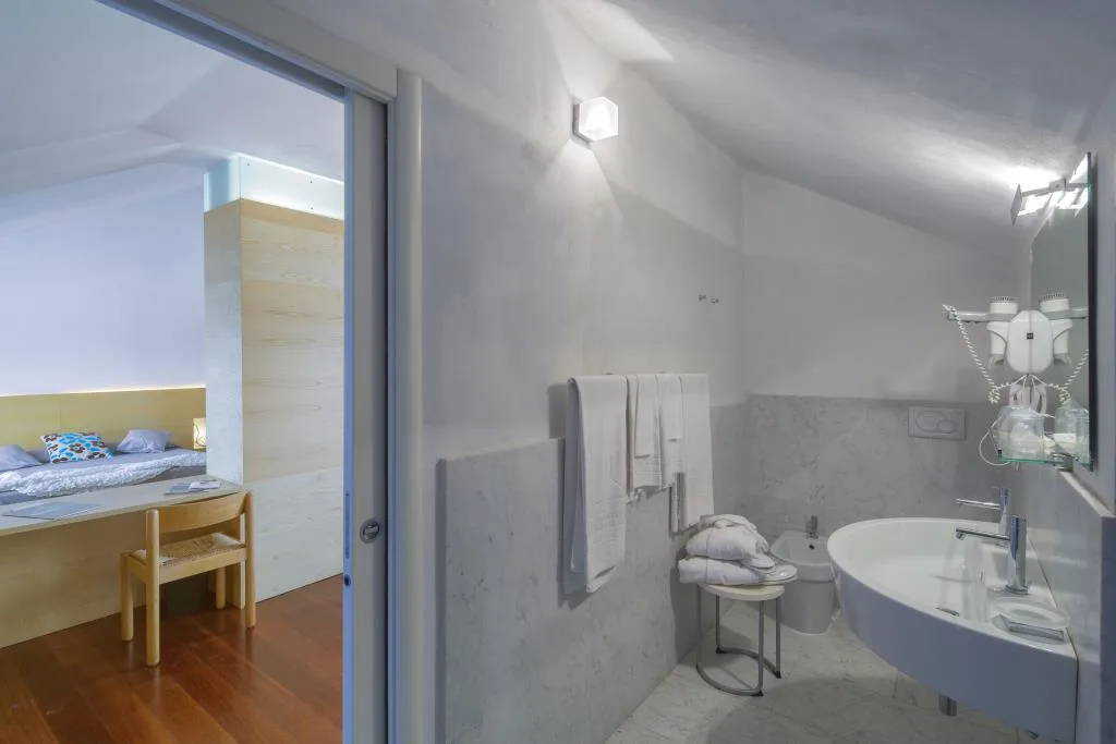 Bagno moderno con lavabo, bidet e rivestimenti chiari, comunicante con la camera da letto