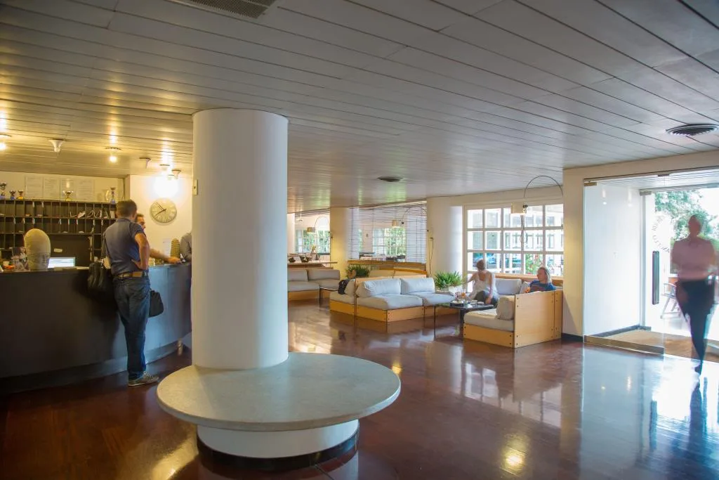 Hall dell'hotel con reception, colonna centrale, divani bianchi e ampie vetrate luminose