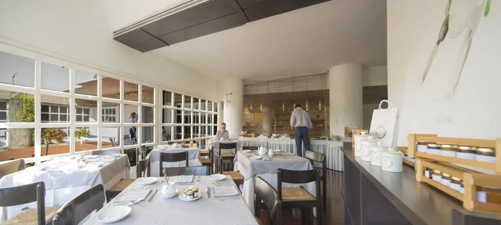 Sala colazione luminosa con tavoli apparecchiati, buffet e grandi vetrate sul giardino