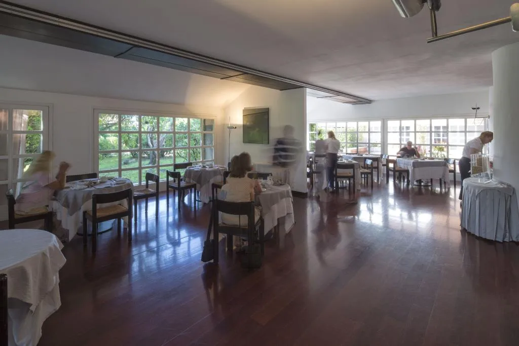 Sala ristorante con ospiti ai tavoli, pavimento in parquet e ampie finestre affacciate sul verde