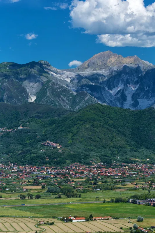 Panorama delle Alpi Apuane con cave di marmo, colline verdi e paese ai piedi delle montagne
