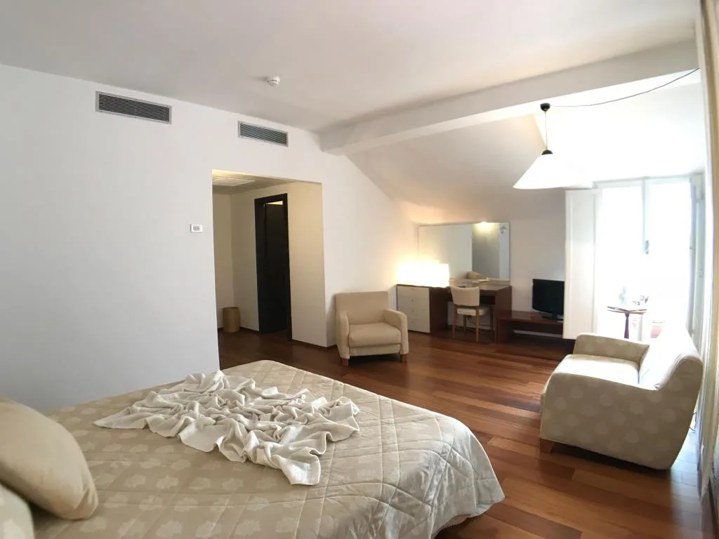 Camera spaziosa con letto matrimoniale, poltrone, scrivania e pavimento in parquet lucido