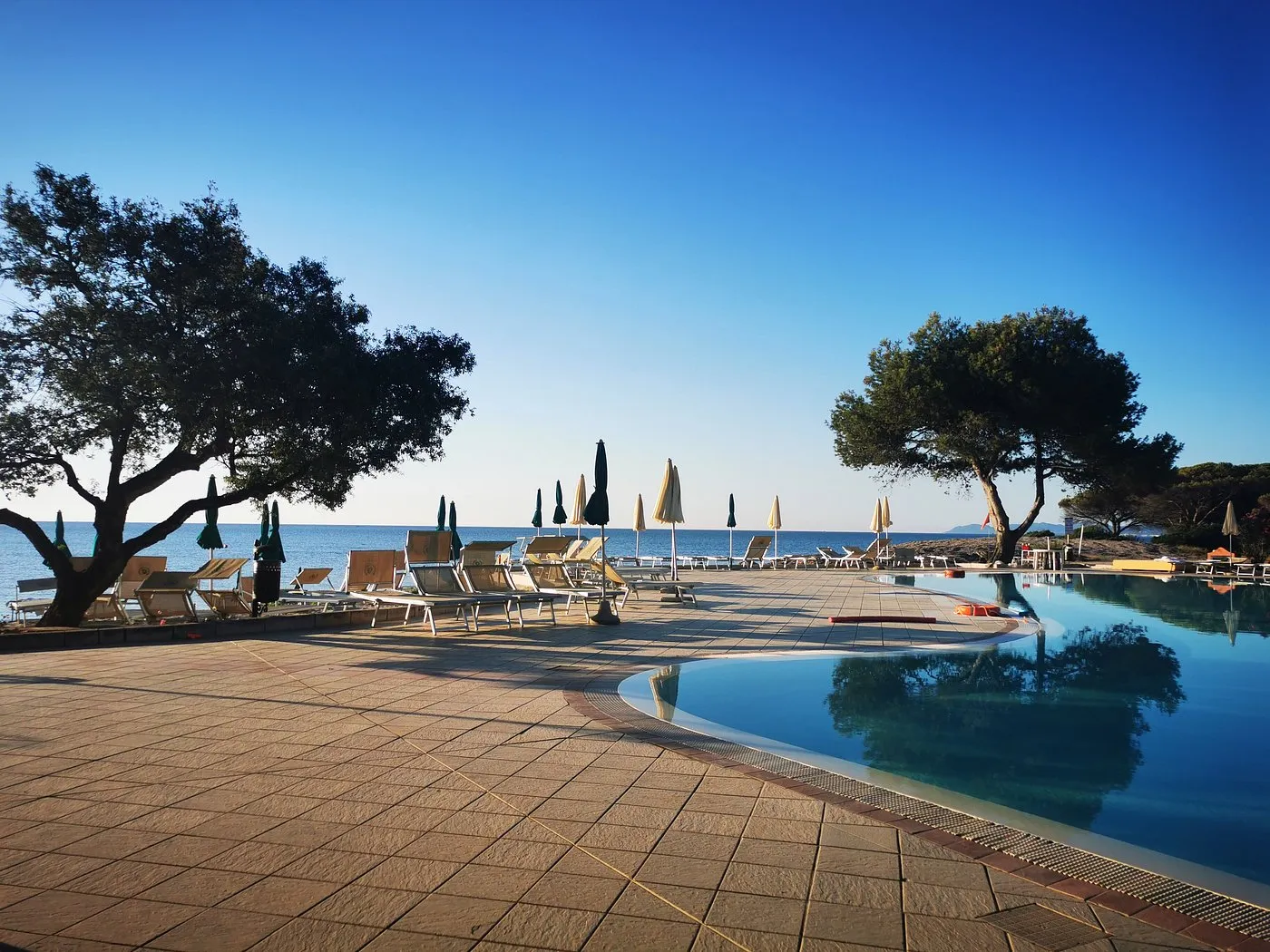 Piscina al tramonto con lettini e alberi affacciata sul mare
