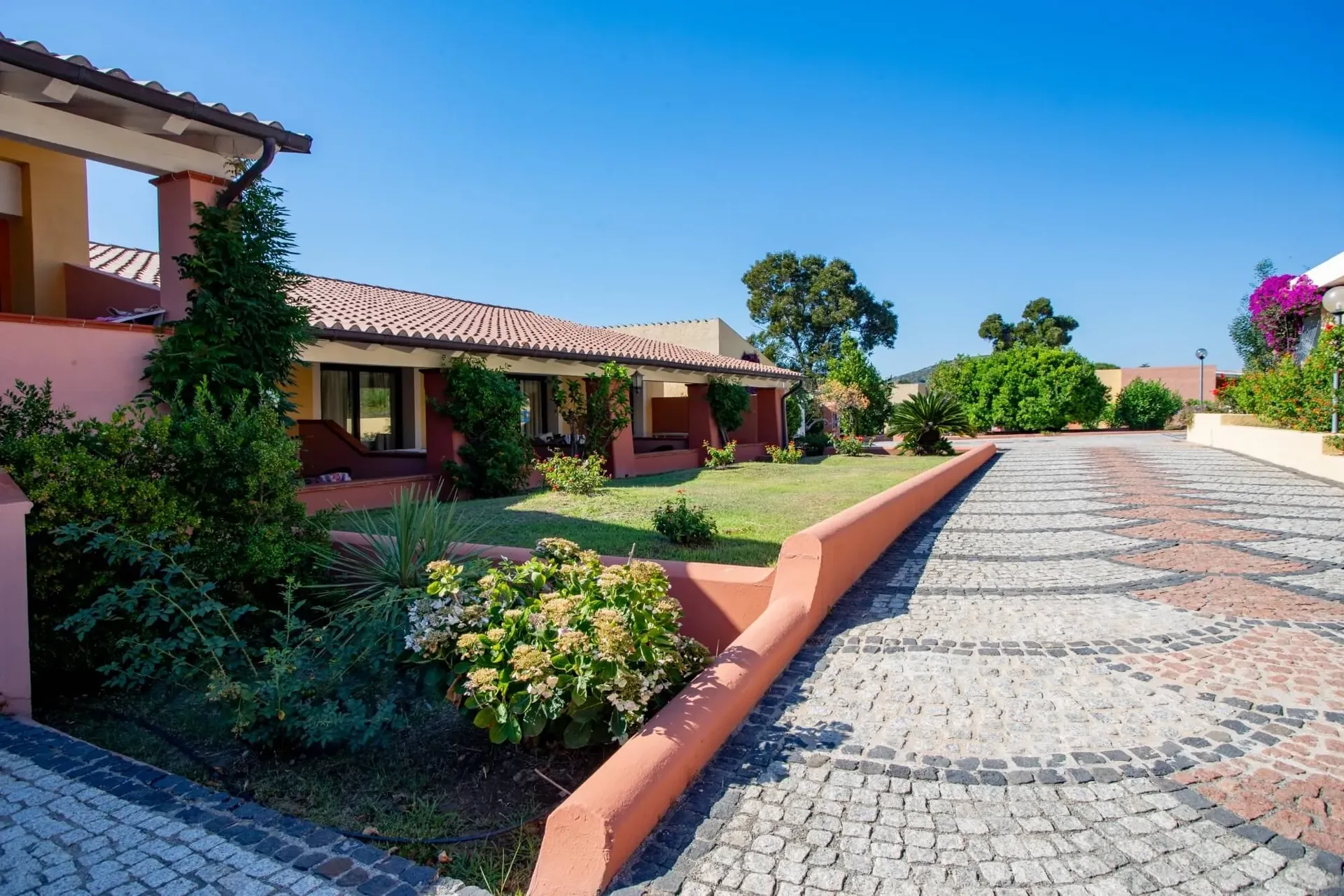 Vialetto pavimentato con giardini fioriti e bungalow mediterranei
