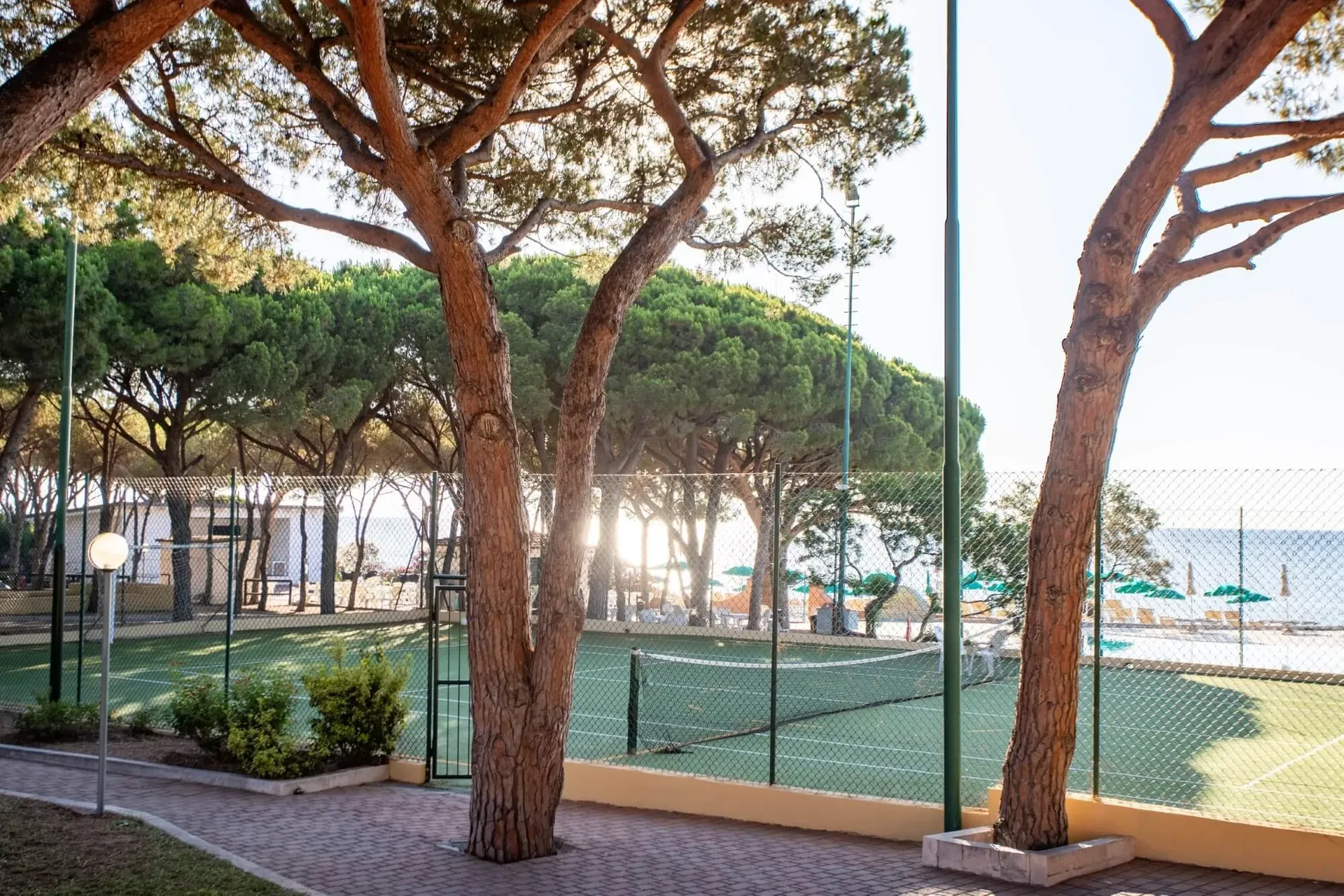 Campo da tennis tra i pini con vista sulla piscina e sul mare al tramonto
