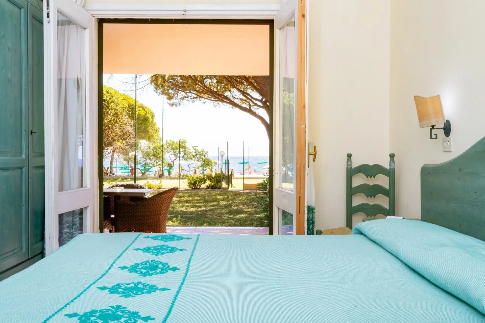 Camera con letto e tessuti verde acqua e vista sul mare dalla porta finestra