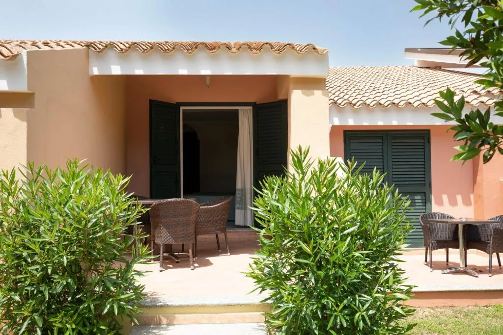 Veranda di un bungalow con tavolo, sedie e siepi verdi