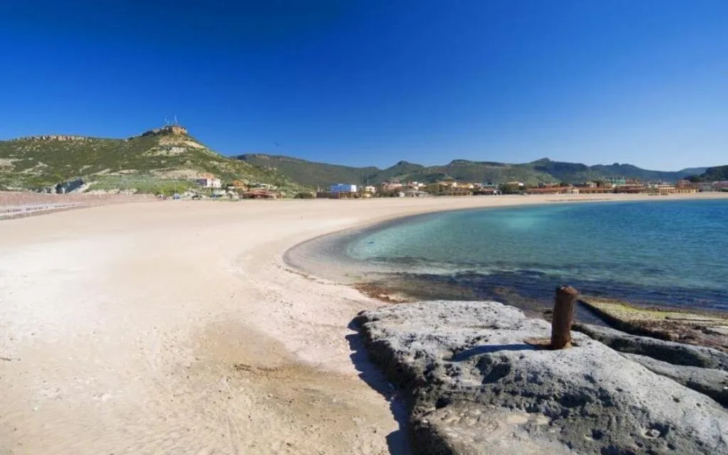 Spiaggia di sabbia chiara con mare limpido e colline sullo sfondo