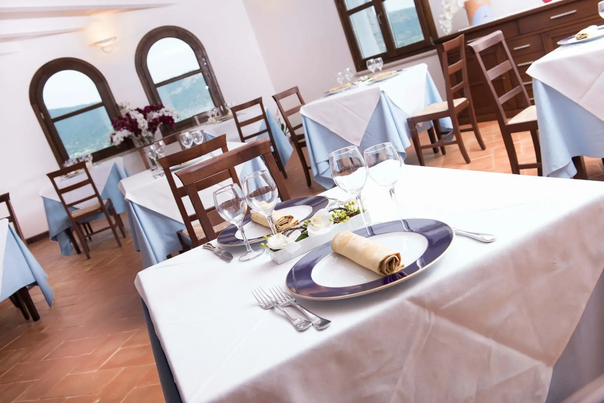 Tavolo da ristorante apparecchiato con piatti blu e vista sulle colline dalle finestre ad arco