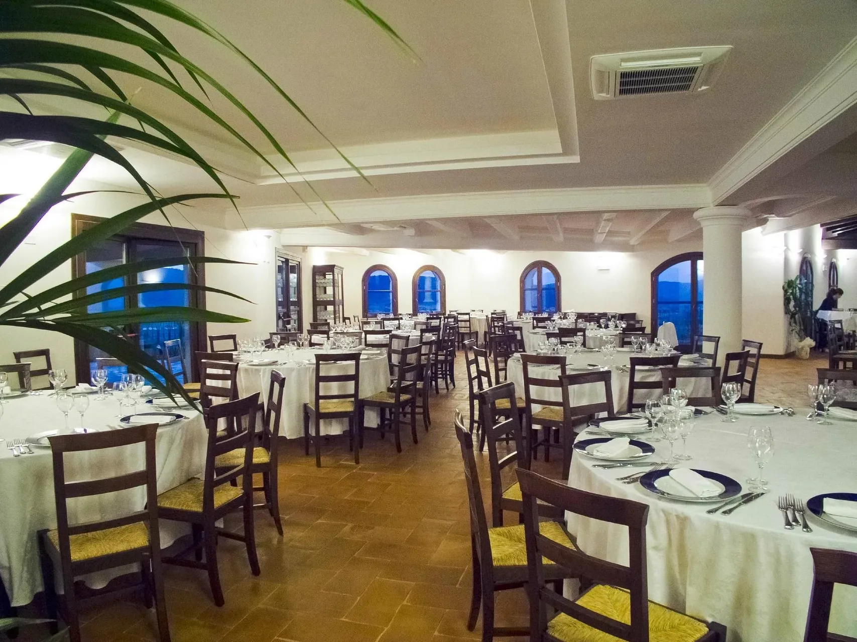 Sala ristorante interna con tavoli rotondi apparecchiati e finestre ad arco