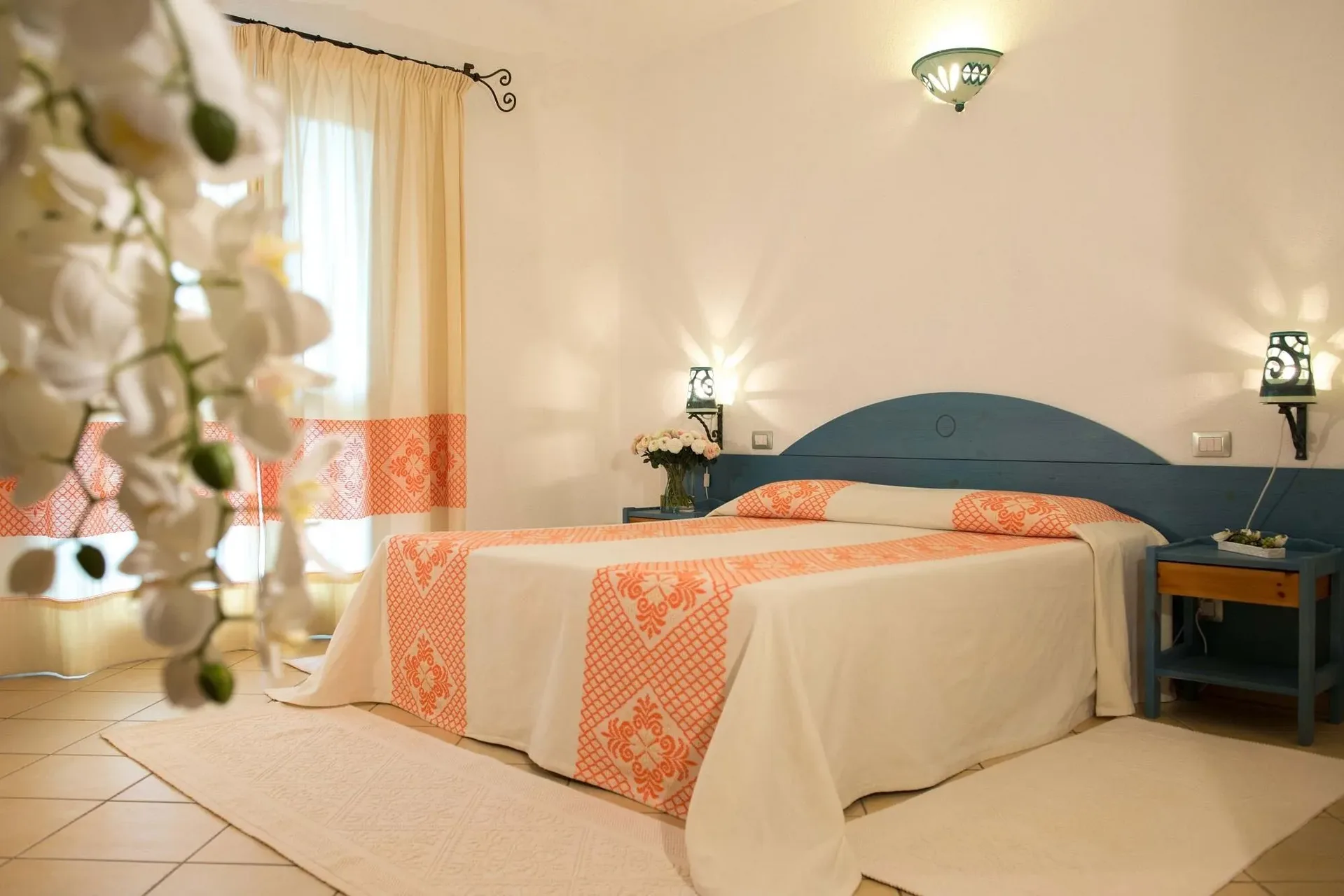 Camera da letto con testiera azzurra, copriletto arancione e orchidea bianca