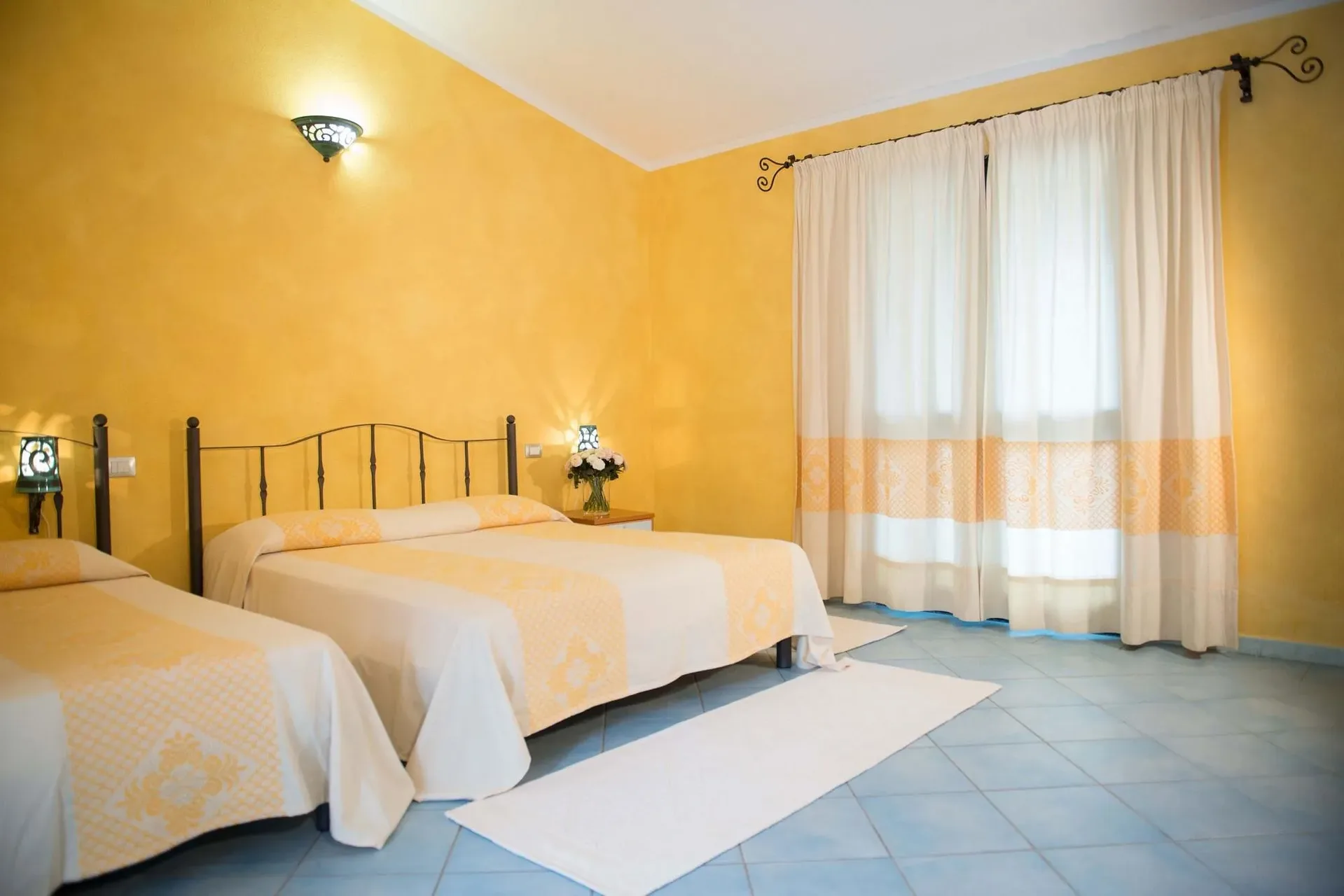 Camera da letto con pareti gialle, due letti e tendaggi bianchi e arancioni