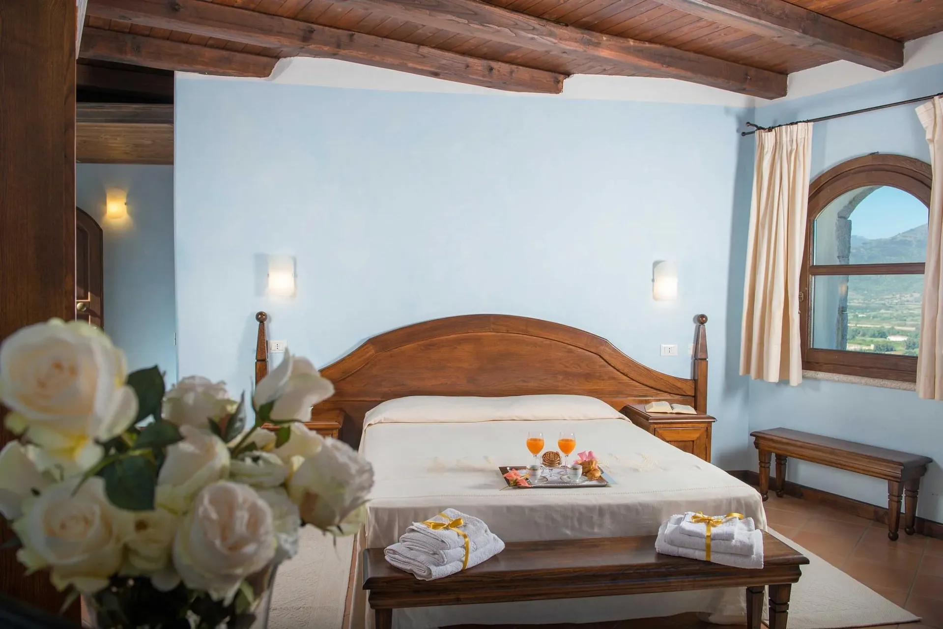 Camera matrimoniale con pareti azzurre, soffitto in legno e vista sulle montagne dalla finestra