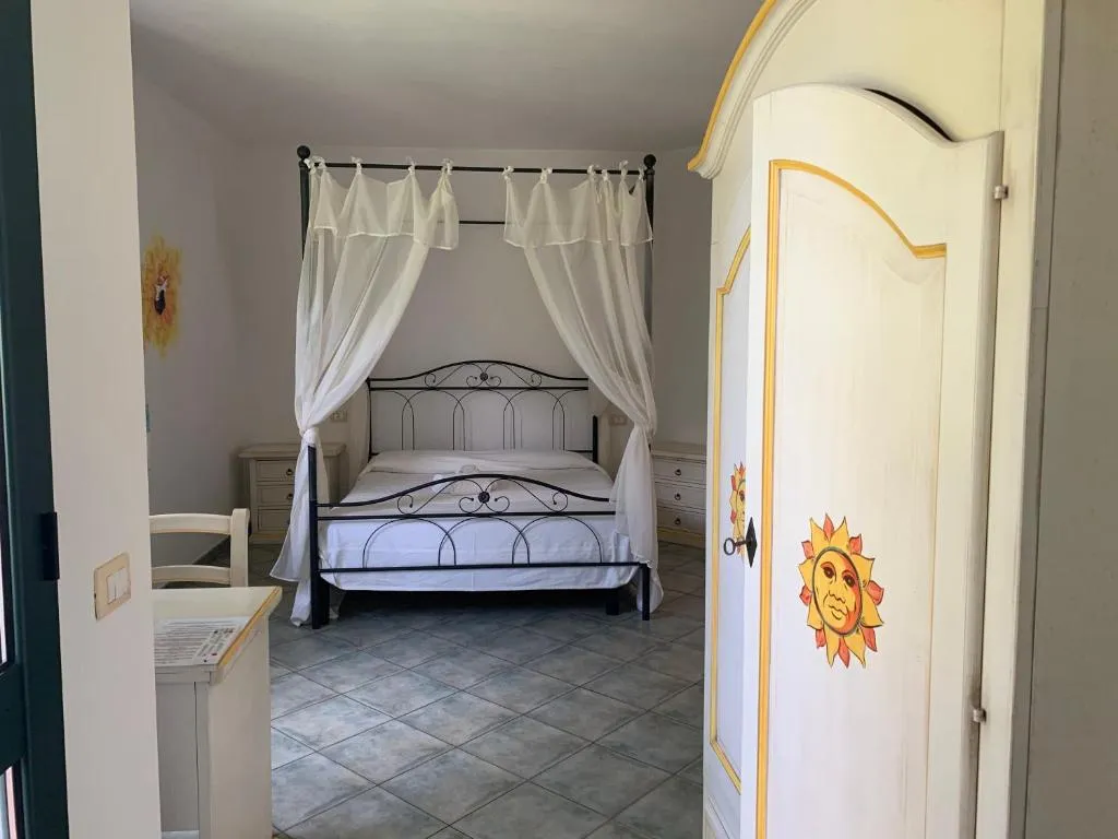 Camera da letto con letto a baldacchino, tende bianche, pavimento in piastrelle e armadio decorato con sole