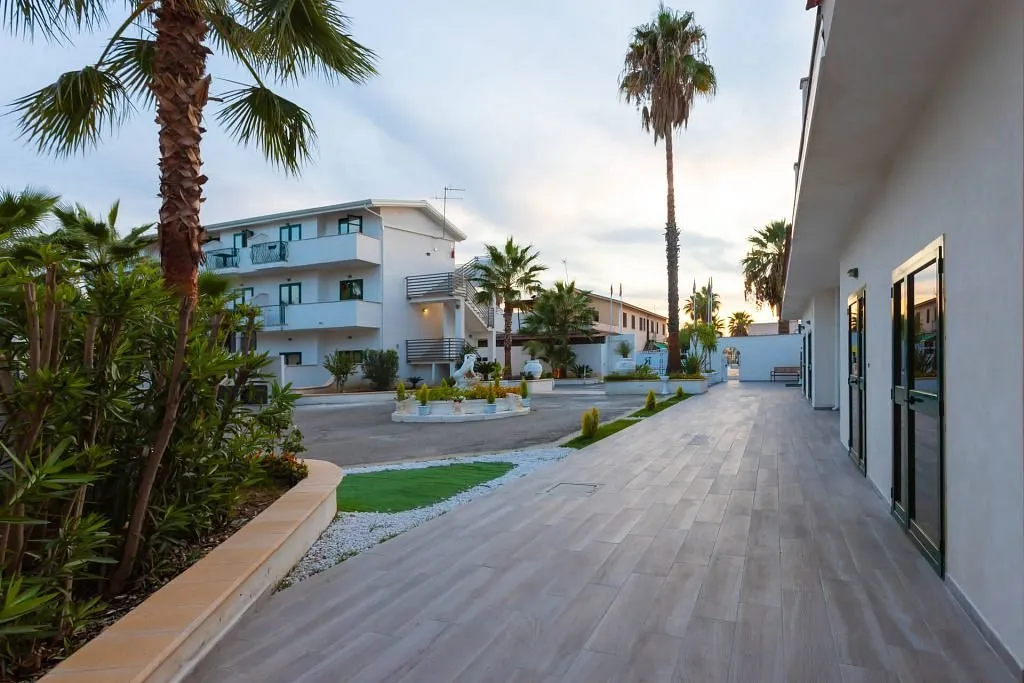 Vialetto pedonale del residence con palme e edifici bianchi al tramonto
