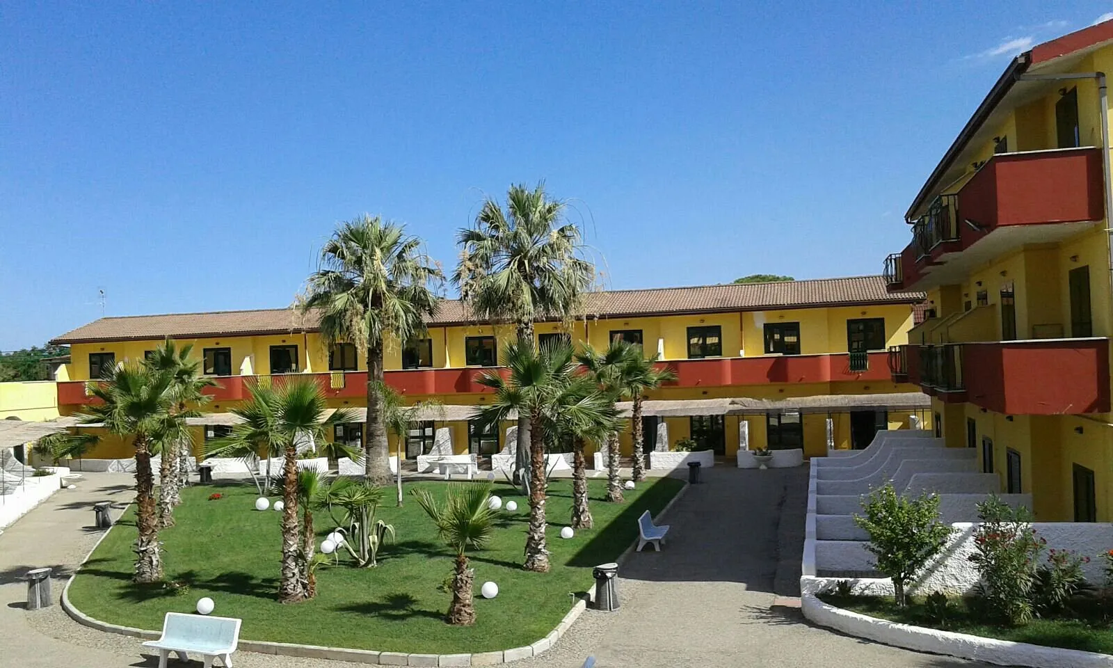 Edificio giallo e rosso del residence con cortile interno e palme